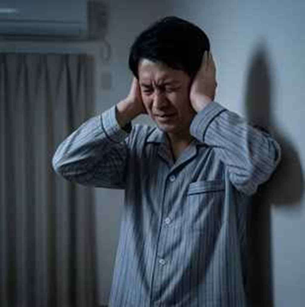  隣人の騒音に悩み耳を塞いで苦痛の表情を浮かべる男性 