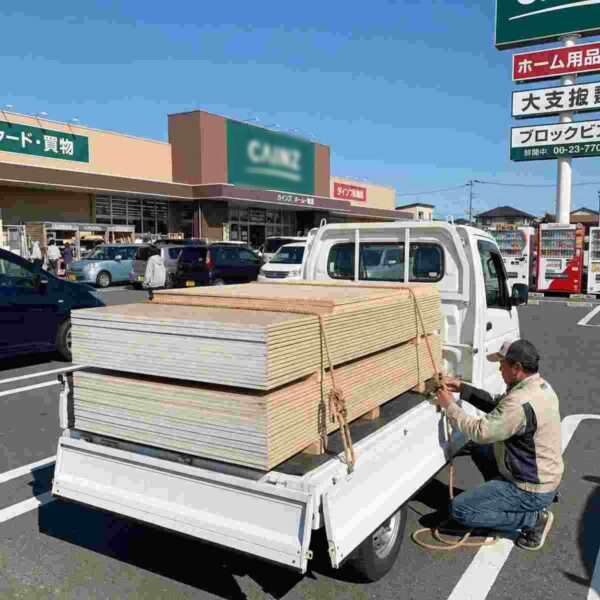 ホームセンターの駐車場で軽トラックに石膏ボードと合板を積み込む男性