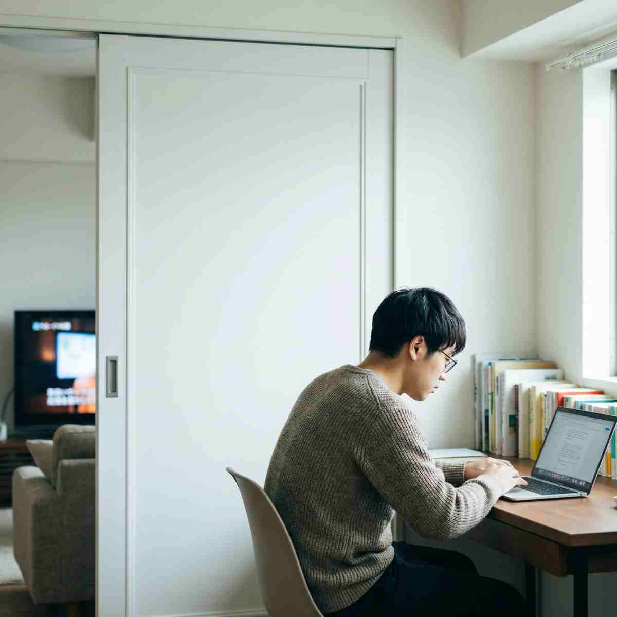 防音引き戸を閉めた書斎でノートPCに集中してテレワークする20代男性