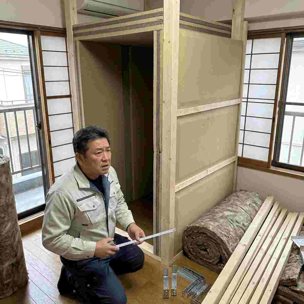 日本の住宅室内でDIY防音室の骨組みの床荷重をメジャーで確認する男性