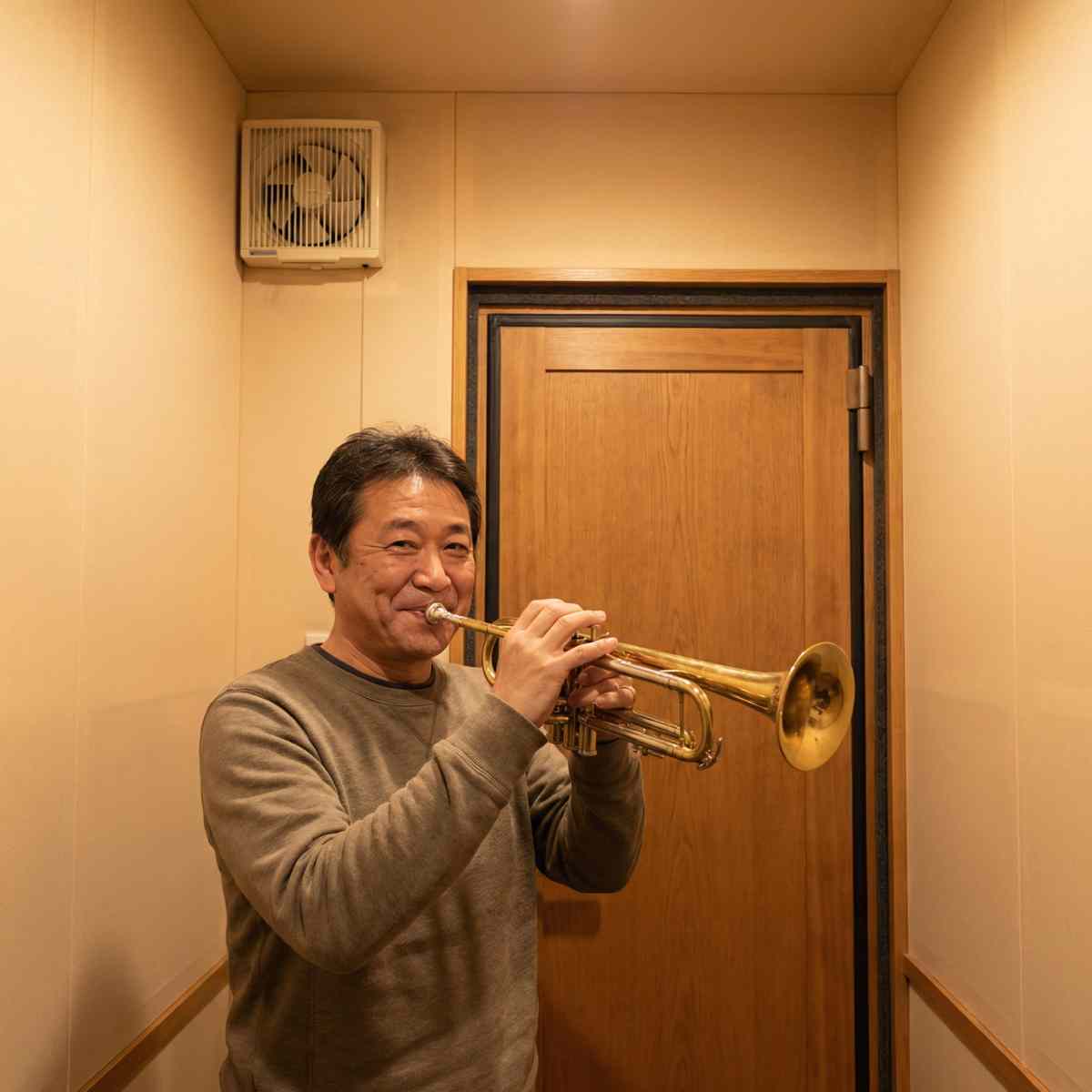 完成したDIY防音室の中でトランペットを演奏する男性。壁には換気扇と防音ドアが設置されている
